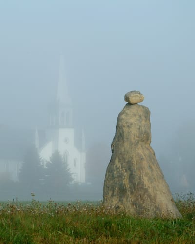Les Amis du Patrimoine de Saint-Venant-de-Paquette - Two stone sculptures, with a church in the background