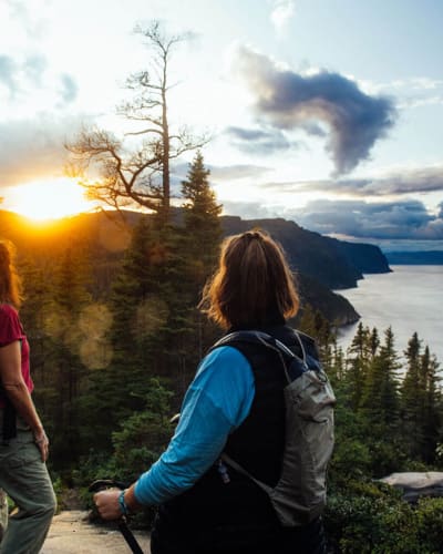 Parc national du Fjord-du-Saguenay - Two women on top of a mountain, forest and sunset in the background.