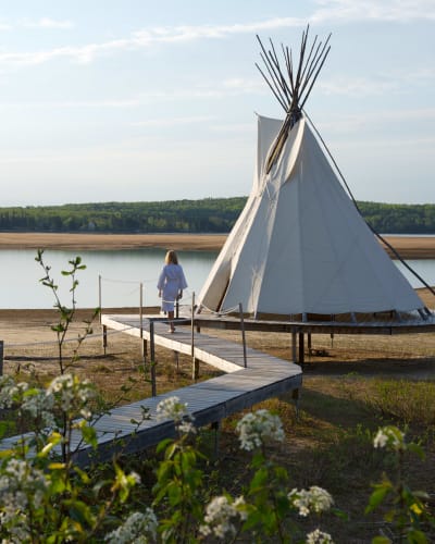 Femme marchant en peignoir marchant à côté d'un tipi sur le bord d'un lac en été.