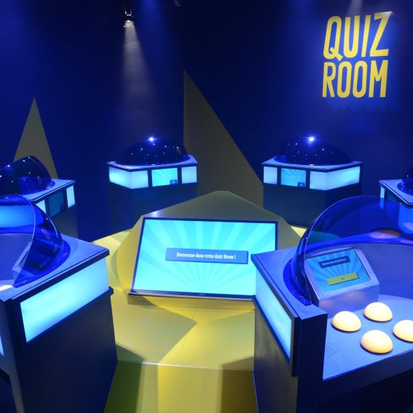 La Boîte à Questions – Quiz Room Montréal - Salle de jeux illuminée avec avec des stations individuelles équipées d'un écrans et boutons.