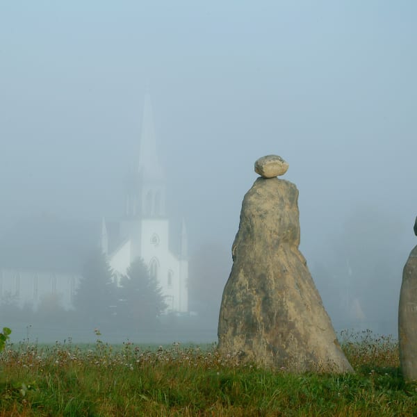 Les Amis du Patrimoine de Saint-Venant-de-Paquette - Two stone sculptures, with a church in the background