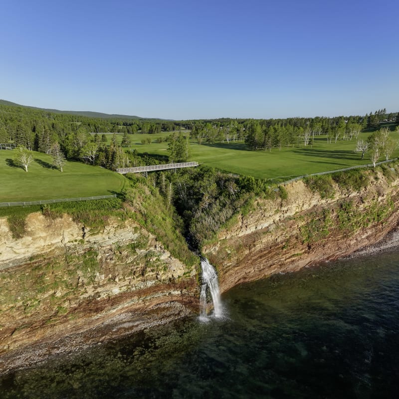 Aux limites d'un terrain de golf verdoyant, un plan d'eau rencontre une falaise rougeâtre. 