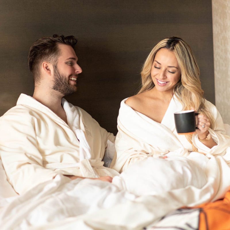 Couple relaxant au lit en peignoirs avec une tasse de café.