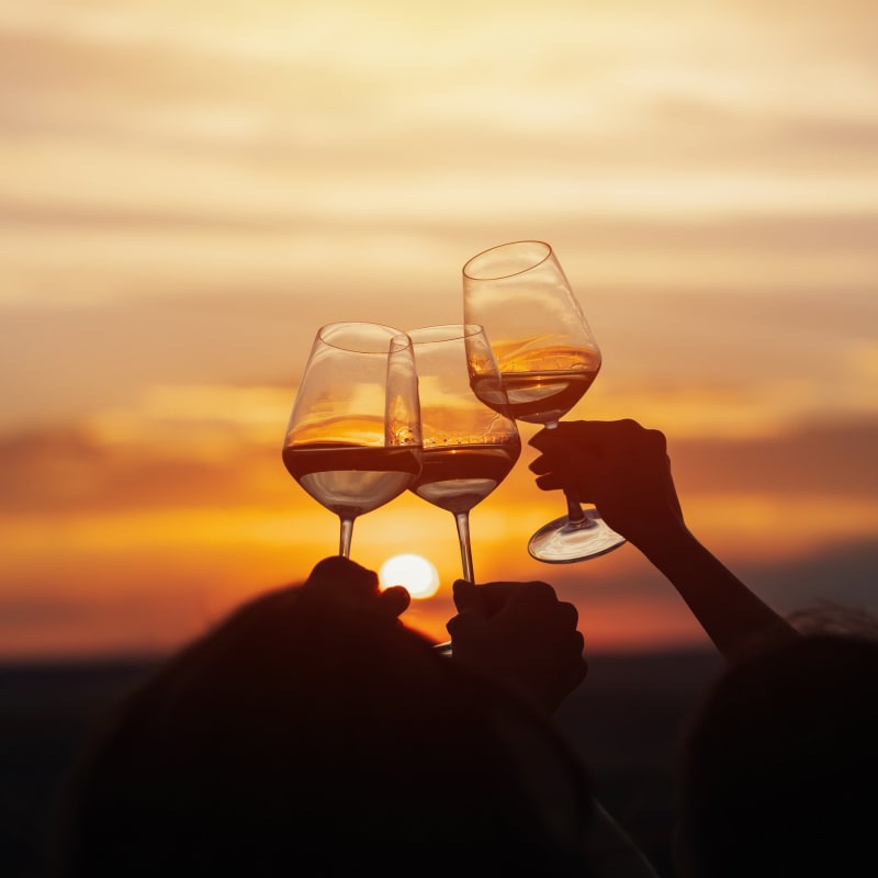 Trois verres de vin levés devant un coucher de soleil