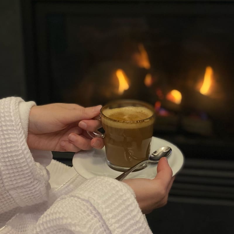 Femme en peignoir avec un café dans les mains devant un foyer.