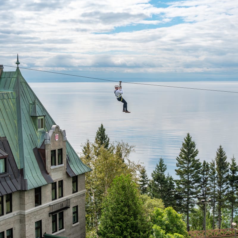 Personne en tyrolienne au dessus du Fairmont Le Manoir Richelieu, avec le fleuve en arrière-plan.