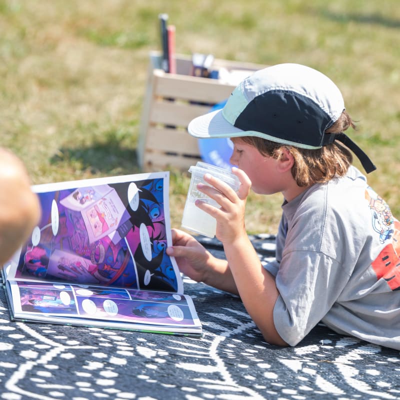 A boy lying on a blanket, reading a comic book