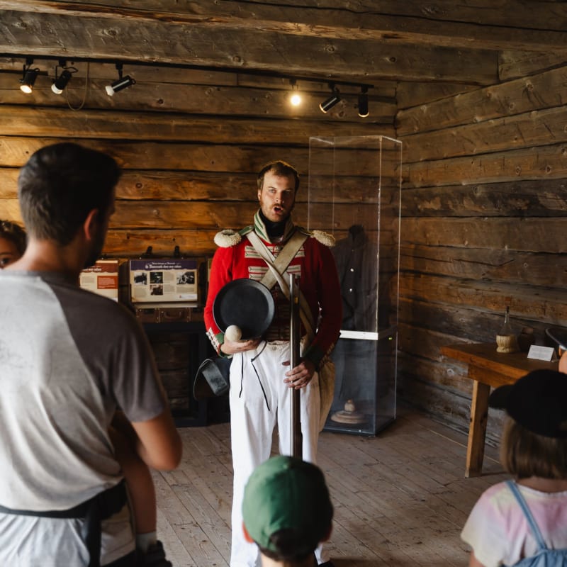 Soldat en uniforme qui se tient devant une famille dans un ancien bâtiment en bois.