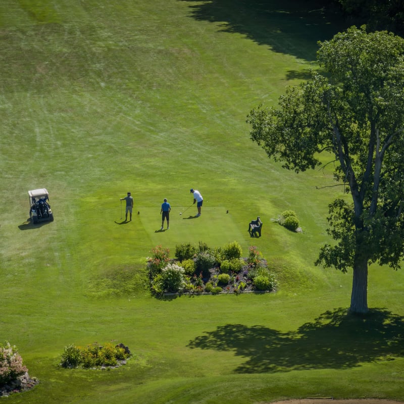 Trois golfeurs et deux voiturettes vus de haut sur un tertre de départ à La Cache du Lac Champlain.