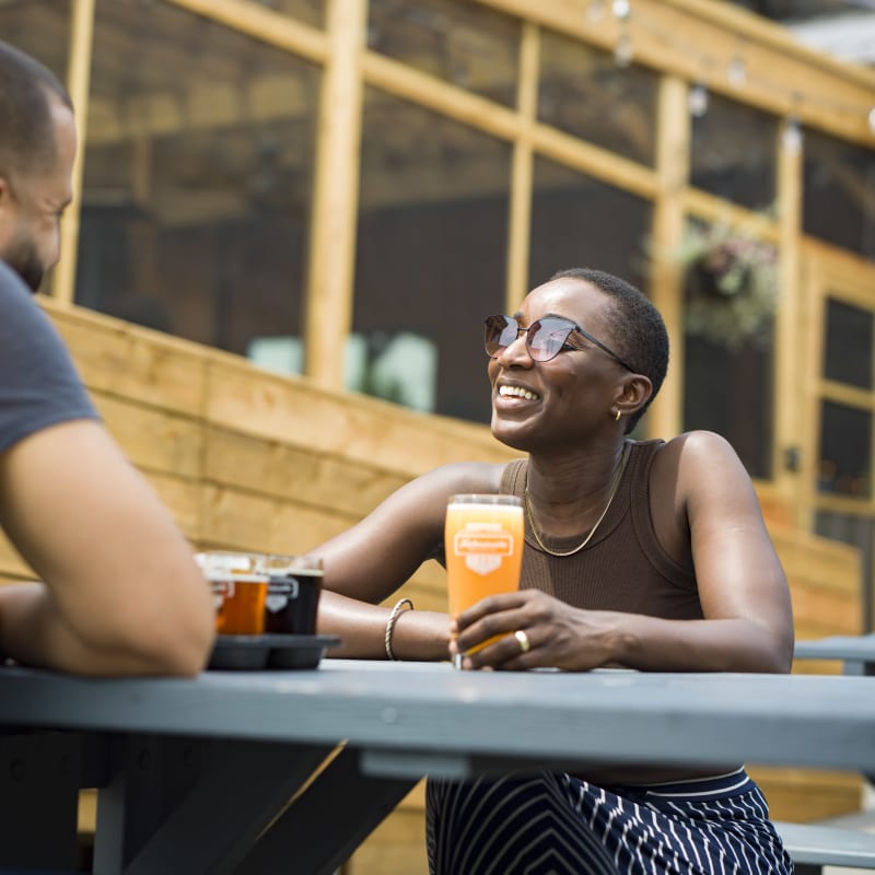 Femme assise à une table extérieure en train de prendre une bière à la Microbrasserie Kahnawake.