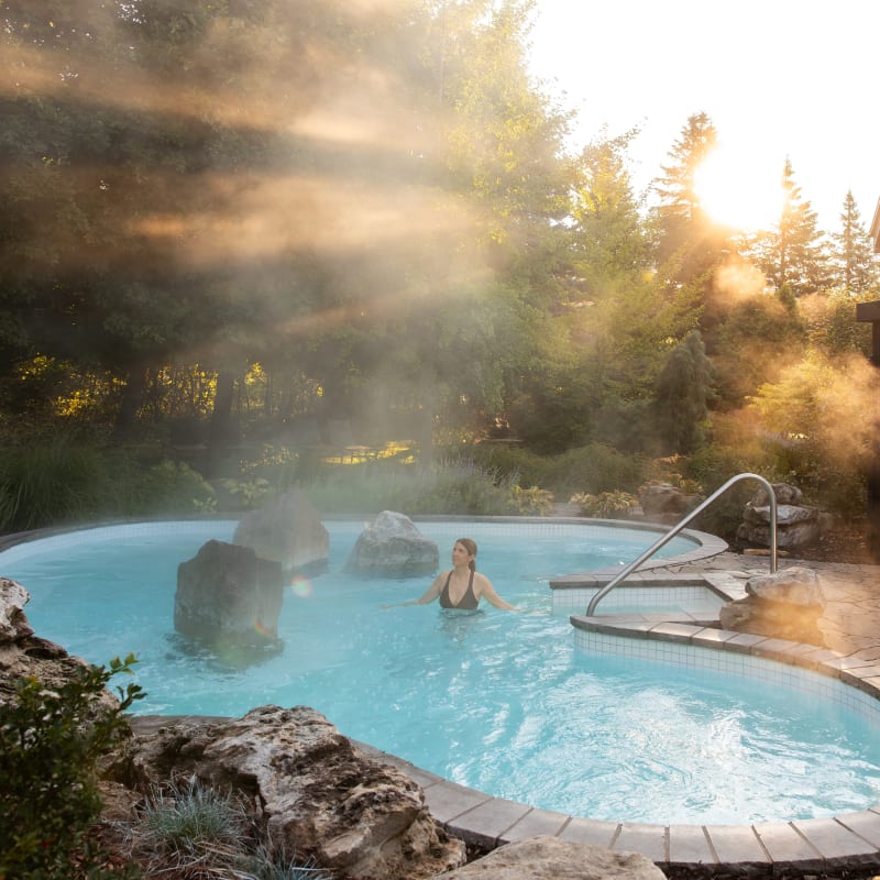 Femme dans un bain thermal au Strom spa nordique Mont-Saint-Hilaire; la scène est baignée d'une lumière dorée.