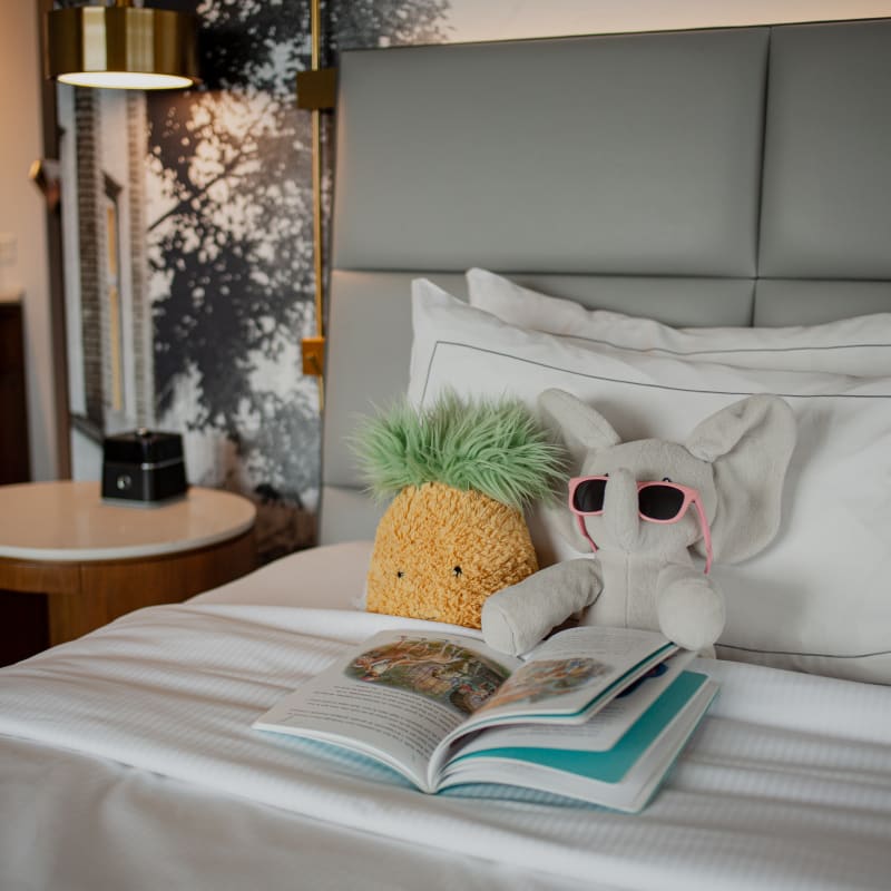 Des peluches sur un lit d’hôtel du Hilton Québec avec un livre pour enfants.