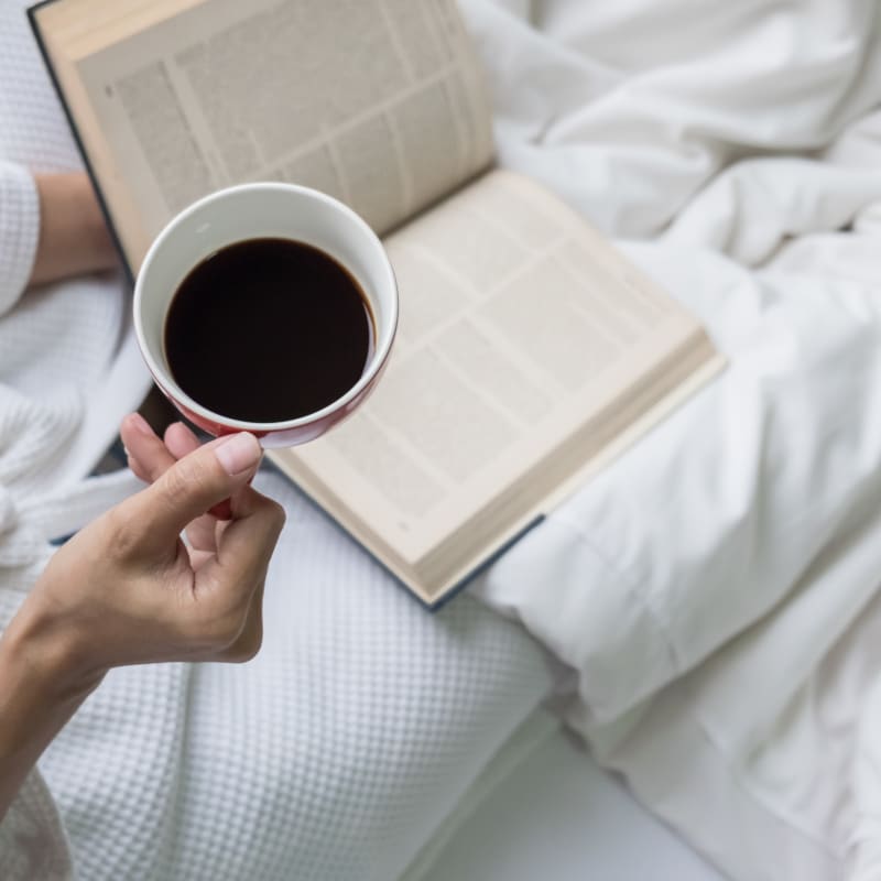 Femme couchée dans un lit avec une tasse de café.