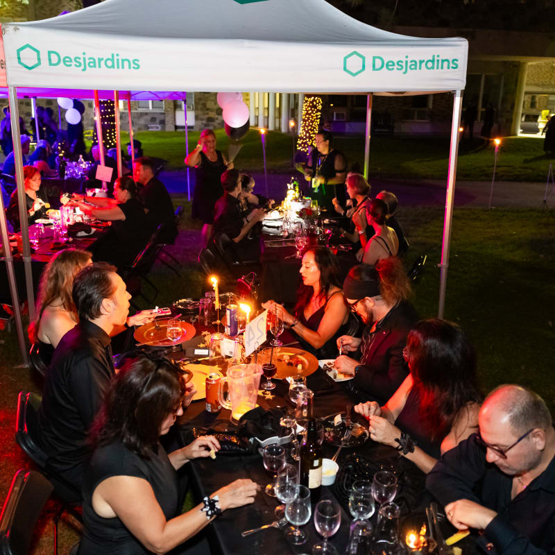 Groups of people dressed in black, seated at a long outdoor table