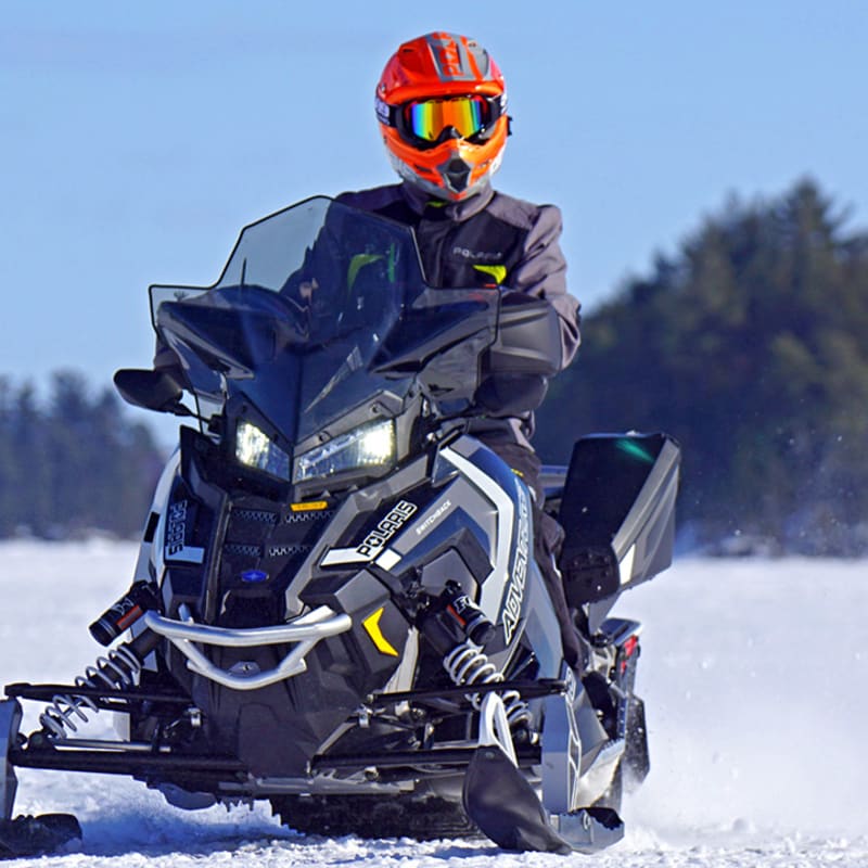 Motoneigiste sur sa motoneige sur la neige avec la forêt derrière.