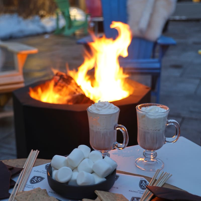 Feu extérieur avec des tasses de chocolat chaud et les ingrédients pour faire des s'mores.