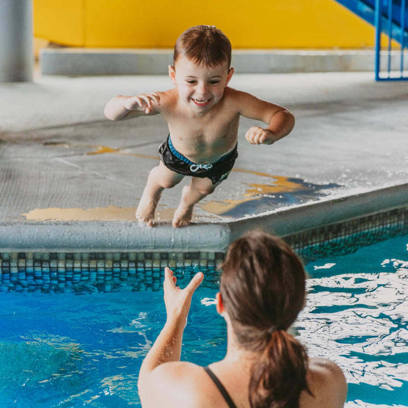 Mère dans la piscine d'hôtel qui attrape son fils qui saute dans l'eau.