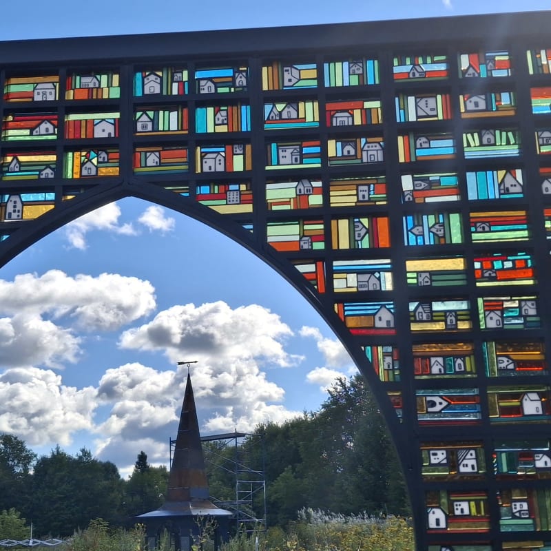 Installation artistique extérieure de plusieurs images en vitraux assemblées pour former un paysage rural.